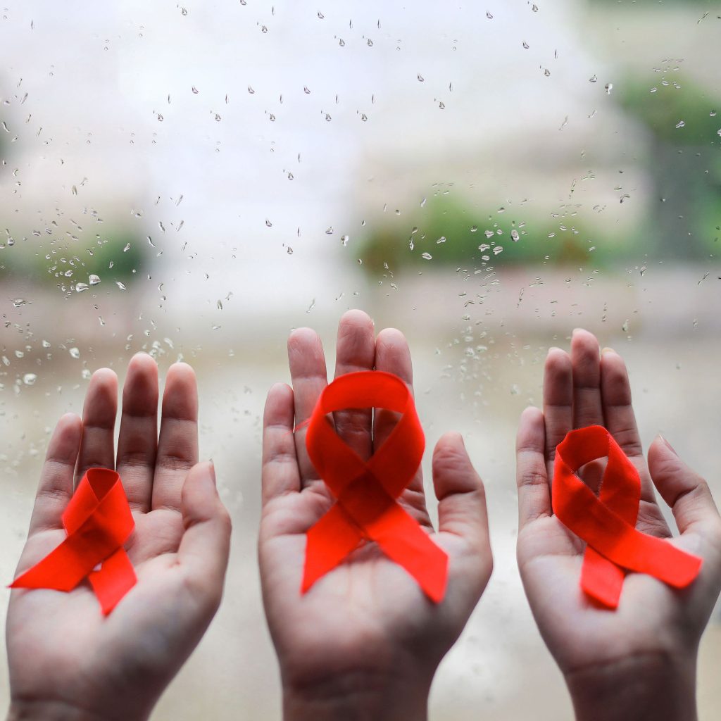 Three hands each holding a red ribbon in front of a damp window that looks outside.